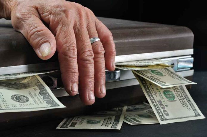 Hand closing briefcase with money sticking out.