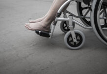 Person's feet in a wheelchair on concrete surface.