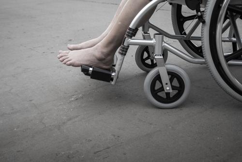 Person's feet in a wheelchair on concrete surface.