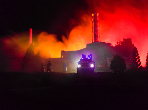 Firefighters and vehicle in front of intense factory blaze.