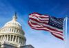 U.S. Capitol building with American flag waving in foreground.