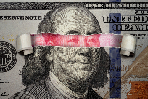 Torn dollar revealing Chinese yuan behind Benjamin Franklin's eyes.