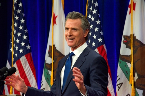 Man speaking at podium with American and California flags.