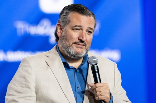 Man in beige blazer holding microphone with blue background.