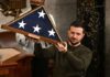 Man holding folded American flag in wooden case.