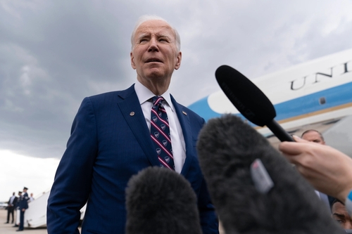 Man in blue suit speaking to microphones near airplane.