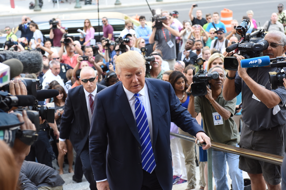 Man in suit surrounded by journalists and cameras