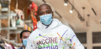 Man wearing Vaccine and Testing hoodie, pointing at text.