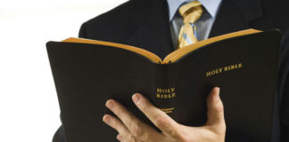 Man in suit holding an open Holy Bible.