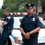 NYPD Killer Cop Sentenced — 11,000 Officers RAGE… Two NYPD officers standing near a police car in an urban environment