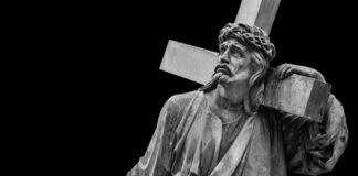A black and white statue of Christ carrying a cross with a sorrowful expression