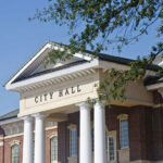 Mayor’s Secret Affair Sparks 18-Count Indictment! City Hall building with columns and a tree branch.