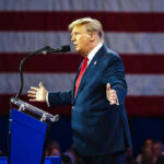 Trump’s ‘Threat’ to Fox Reporter—Truth Revealed! Man speaking at podium with American flag backdrop.