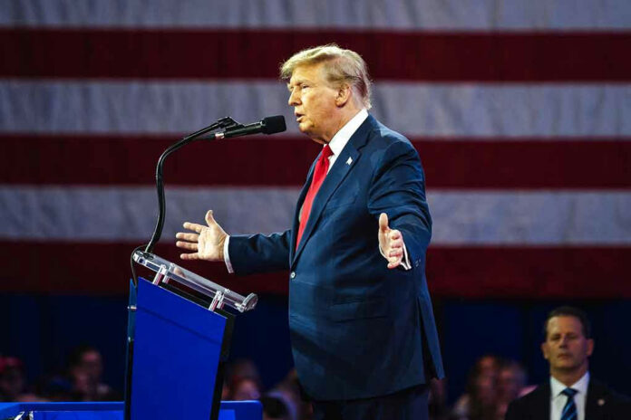 2455398299 Man speaking at podium with American flag backdrop.