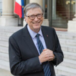 Man in suit outside building, flag in background.