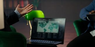 Person gesturing towards a laptop displaying a world map and data analytics