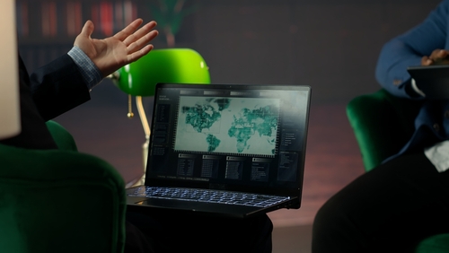 shutterstock_2577465565.jpg Person gesturing towards a laptop displaying a world map and data analytics