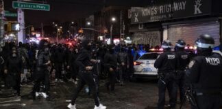 Crowd of people gathered on a street with police officers and vehicles