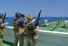 Armed security team on a ship deck overlooking a large tanker at sea