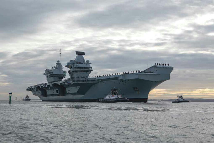1254447181 Aircraft carrier with tugboats on a cloudy sea.