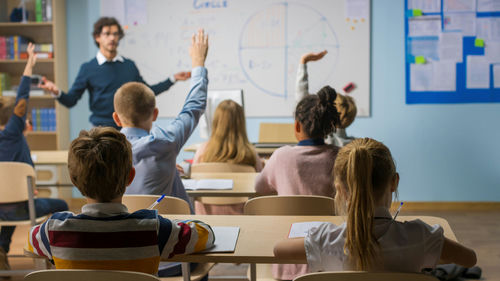 shutterstock1767334112jpg Students raising hands in a classroom as a teacher leads a lesson