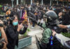 protester faces riot police amid crowd with cameras and masks
