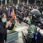 NYC’s Protest Law Has One Major Exception protester faces riot police amid crowd with cameras and masks
