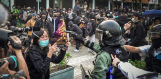 protester faces riot police amid crowd with cameras and masks