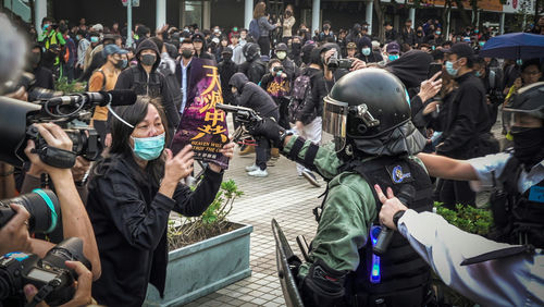 shutterstock1831321549-1jpg protester faces riot police amid crowd with cameras and masks