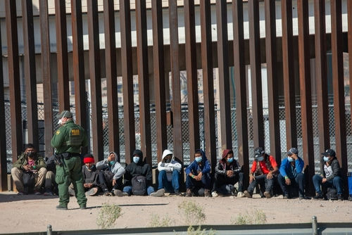 shutterstock2079408463-1jpg Border patrol agent with group of seated immigrants.