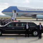Presidential motorcade limousine in front of large government aircraft on tarmac