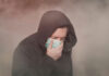 See The Worldâs Dirtiest Air Person with hood and mask coughing in foggy setting.
