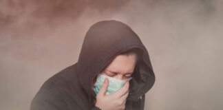 Person with hood and mask coughing in foggy setting.