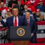two men at a podium during a large indoor rally