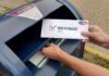 Ballot Blockade: USPS Draws a Line Person mailing a ballot into a blue street mailbox