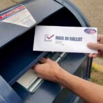Person mailing a ballot into a blue street mailbox
