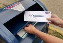 Ballot Blockade: USPS Draws a Line Person mailing a ballot into a blue street mailbox