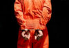 Repeat Offender Ends Up in Governor’s Backyard Person in orange jumpsuit handcuffed behind their back.