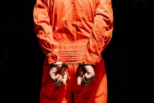 shutterstock_2190108267 Person in orange jumpsuit handcuffed behind their back.