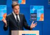 Man in suit speaking at podium with NATO backdrop