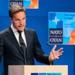 5% Shock: NATO’s Pricey New Pledge Man in suit speaking at podium with NATO backdrop