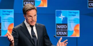 Man in suit speaking at podium with NATO backdrop