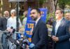 Man in suit speaks at outdoor press conference with microphones