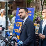 Times Square Ban Sparks Patriotic Brawl Man in suit speaks at outdoor press conference with microphones