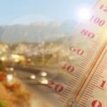Holiday Heat Turns Deadly Fast Close-up of a thermometer in hot sun over a blurred road and mountains