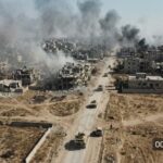 Drone Barrage Rattles Moscow’s Oil Lifeline Aerial view of a war-torn city with smoke rising from buildings