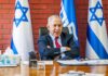 man in suit seated at desk with Israeli flags