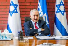man in suit seated at desk with Israeli flags