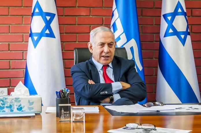 man in suit seated at desk with Israeli flags