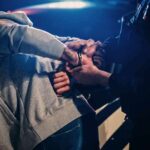 Police officer handcuffing person at night by patrol car